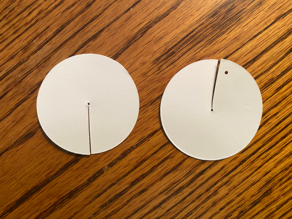 2" circular discs cut from white cardstock, with radii cut through each, one with a 1/16 inch hole punched.